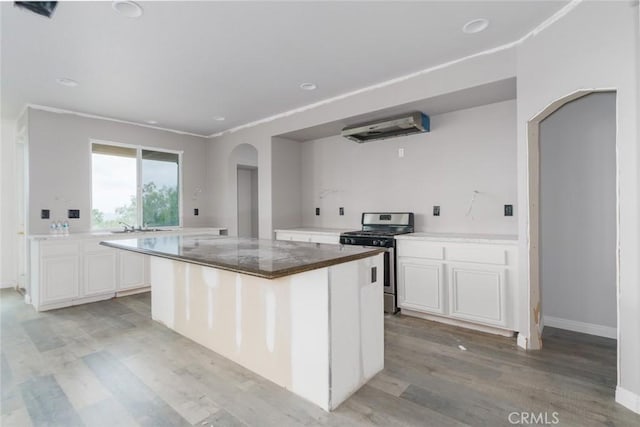 1059 Stowell Ranch Cir, Corona, CA 92881 - kitchen with stainless steel gas range, under cabinet range hood, light wood-style flooring, white cabinetry, and arched walkways