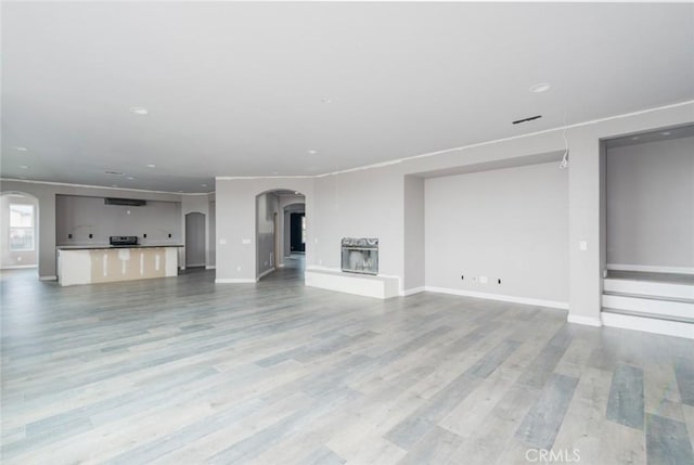 1059 Stowell Ranch Cir, Corona, CA 92881 - unfurnished living room featuring light wood-type flooring, baseboards, a fireplace with raised hearth, and arched walkways