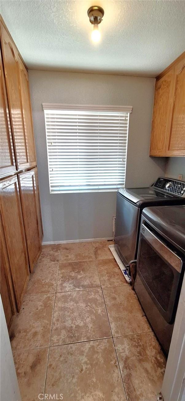 laundry room featuring light tile patterned floors, cabinet space, a textured ceiling, and washing machine and dryer