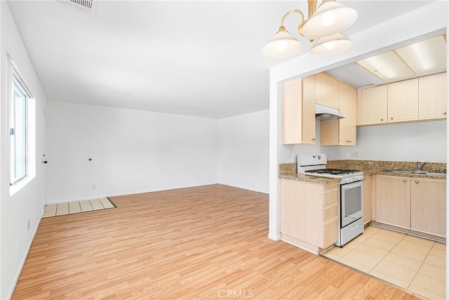 kitchen with light brown cabinetry, a sink, light wood-style floors, gas range gas stove, and open floor plan