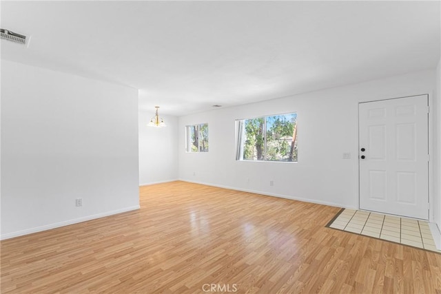 unfurnished living room featuring baseboards, a notable chandelier, light wood-style flooring, and visible vents