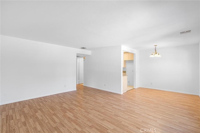 unfurnished room with visible vents, baseboards, a notable chandelier, and light wood-type flooring