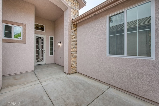 view of exterior entry with stucco siding, a patio area, and stone siding