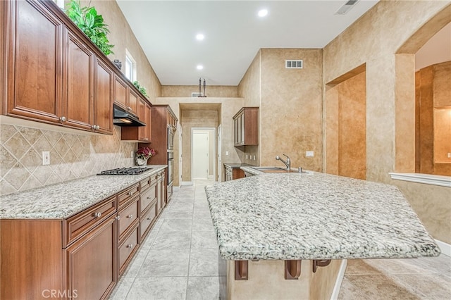 kitchen featuring stainless steel gas cooktop, light stone countertops, a sink, visible vents, and a peninsula