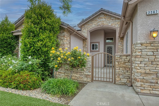 entrance to property featuring stone siding, stucco siding, and a gate