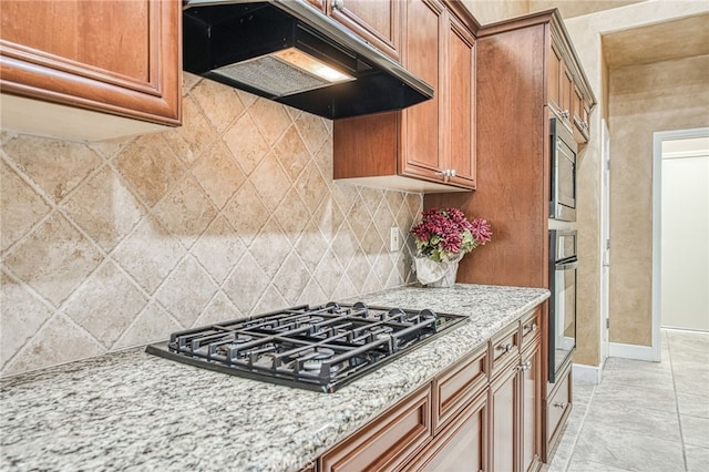 kitchen with brown cabinets, stainless steel appliances, decorative backsplash, and under cabinet range hood