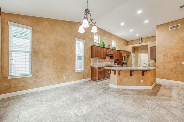 kitchen with visible vents, baseboards, a kitchen bar, light stone countertops, and brown cabinetry