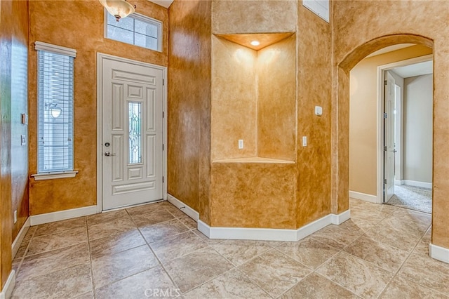 foyer entrance featuring a towering ceiling, baseboards, and arched walkways