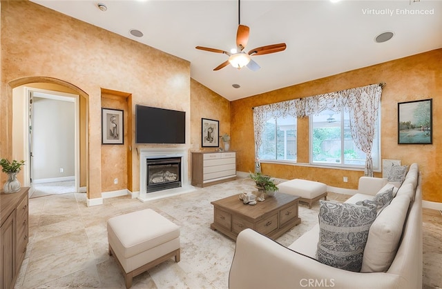 living area featuring baseboards, vaulted ceiling, a ceiling fan, and a glass covered fireplace