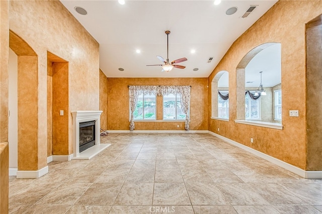 unfurnished living room with a glass covered fireplace, visible vents, a ceiling fan, and arched walkways