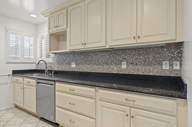 kitchen featuring backsplash, stainless steel dishwasher, a sink, light tile patterned flooring, and cream cabinetry