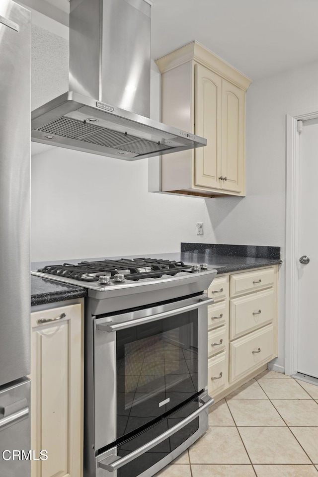 kitchen featuring dark countertops, wall chimney exhaust hood, cream cabinetry, light tile patterned floors, and stainless steel appliances