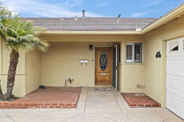 doorway to property with a garage, a shingled roof, and stucco siding