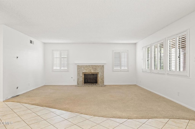 unfurnished living room featuring visible vents, a fireplace, light carpet, baseboards, and a textured ceiling