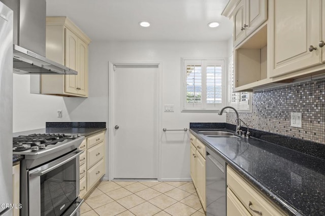 kitchen with wall chimney range hood, cream cabinets, stainless steel appliances, and a sink