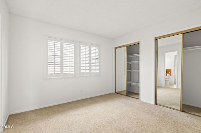 unfurnished bedroom featuring carpet floors, baseboards, and two closets