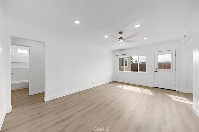 unfurnished living room featuring light wood finished floors, ceiling fan, a wall mounted AC, and baseboards