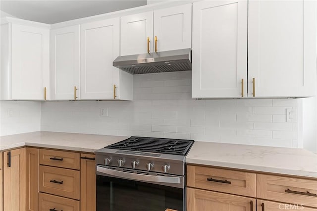 kitchen with light stone countertops, stainless steel gas stove, under cabinet range hood, and tasteful backsplash