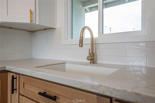 details featuring light stone countertops, a sink, white cabinets, and decorative backsplash