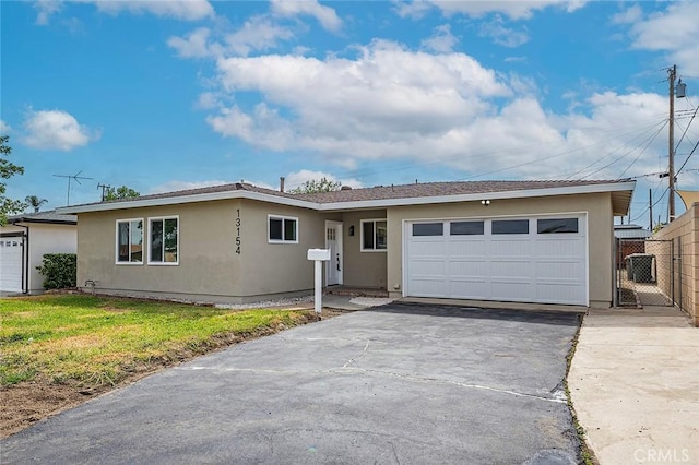 ranch-style home featuring a front yard, stucco siding, aphalt driveway, an attached garage, and fence