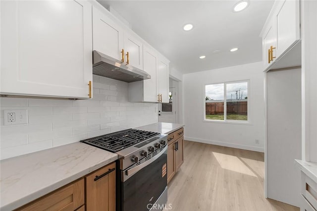 kitchen with stainless steel gas stove, exhaust hood, light wood finished floors, and decorative backsplash