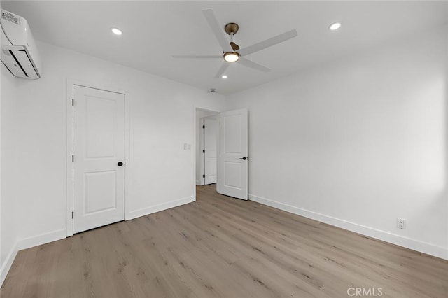 unfurnished bedroom with recessed lighting, a wall unit AC, wood finished floors, and baseboards