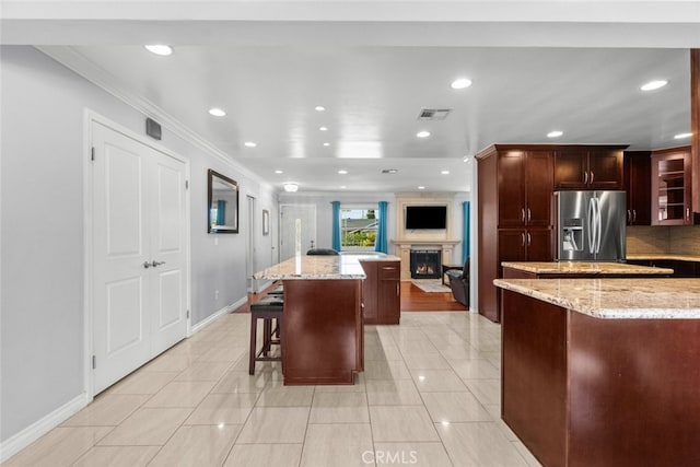 kitchen with recessed lighting, crown molding, visible vents, stainless steel refrigerator with ice dispenser, and a kitchen island