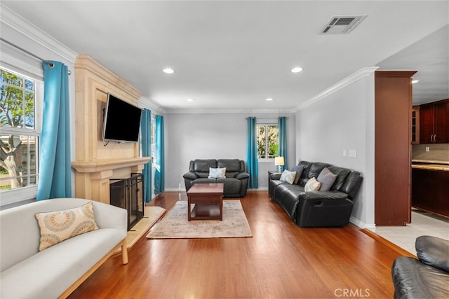 living area featuring a fireplace, light wood finished floors, visible vents, and plenty of natural light