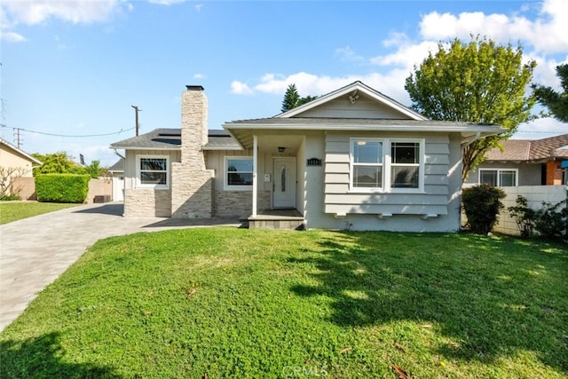 view of front of home with a chimney, fence, solar panels, driveway, and a front lawn