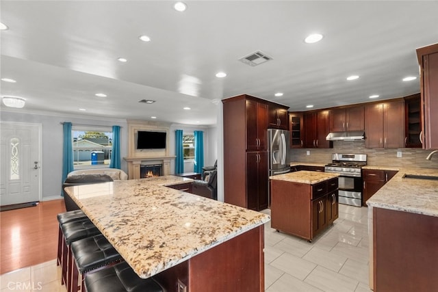 kitchen with a sink, visible vents, stainless steel appliances, a kitchen island, and under cabinet range hood