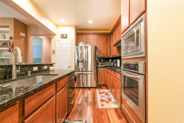 kitchen with tasteful backsplash, a sink, dark stone countertops, light wood finished floors, and stainless steel appliances