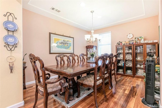 dining space with visible vents, wood finished floors, baseboards, an inviting chandelier, and a tray ceiling