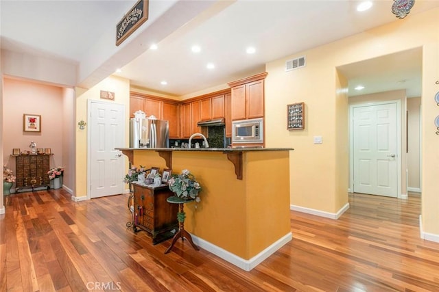 kitchen with light wood finished floors, a breakfast bar area, an island with sink, stainless steel appliances, and visible vents