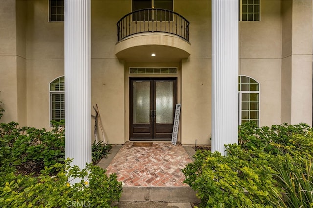 view of exterior entry with a balcony, french doors, and stucco siding