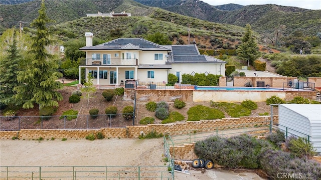 rear view of property with a fenced backyard, a balcony, a chimney, a mountain view, and stucco siding