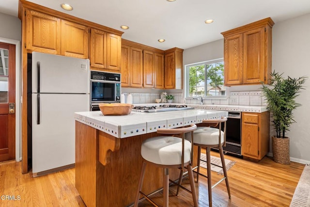 kitchen featuring recessed lighting, light wood-style floors, brown cabinetry, a center island, and black appliances