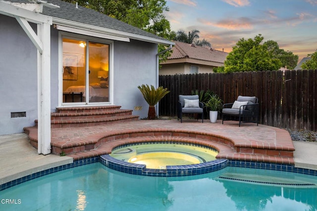 pool at dusk with fence, a patio area, entry steps, and a pool with connected hot tub