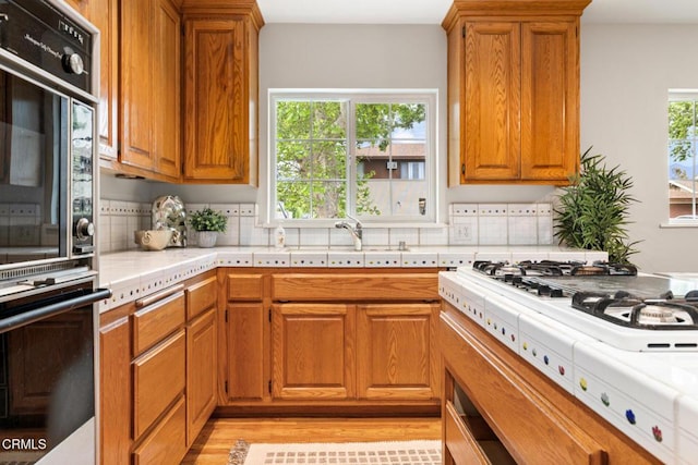 kitchen with a sink, brown cabinets, decorative backsplash, and double oven