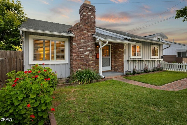 view of front of property featuring a shingled roof, a yard, board and batten siding, a chimney, and fence