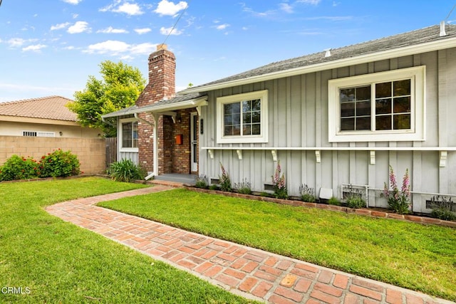 ranch-style house featuring a front lawn, fence, board and batten siding, and a chimney