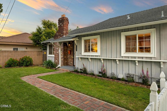 single story home featuring a chimney, board and batten siding, a yard, fence, and a shingled roof