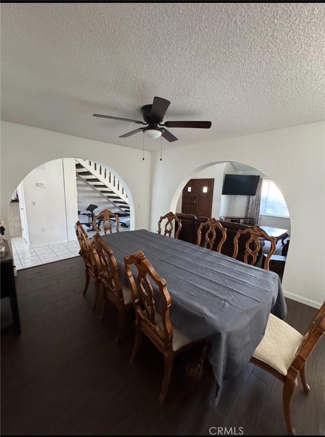 dining room with arched walkways, ceiling fan, wood finished floors, and a textured ceiling