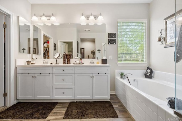 bathroom with double vanity, a sink, wood finished floors, and a garden tub