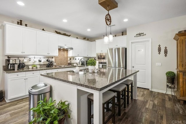 kitchen with white cabinets, appliances with stainless steel finishes, a breakfast bar area, dark wood-type flooring, and under cabinet range hood