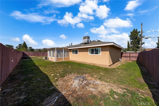 back of house featuring a sunroom, a fenced backyard, a lawn, and stucco siding