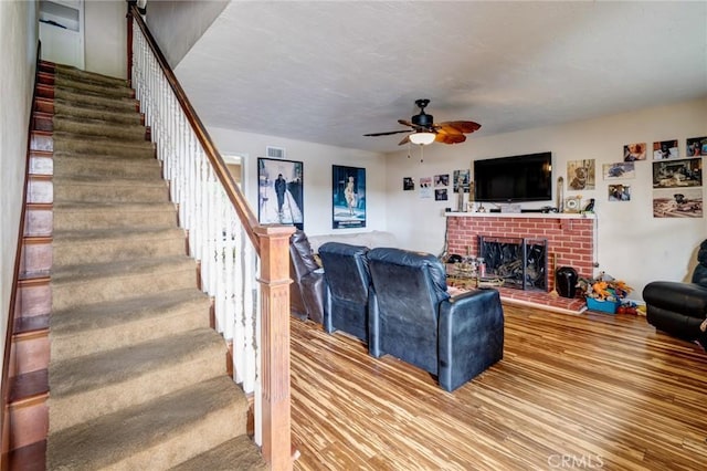 living room with visible vents, stairs, a brick fireplace, wood finished floors, and ceiling fan