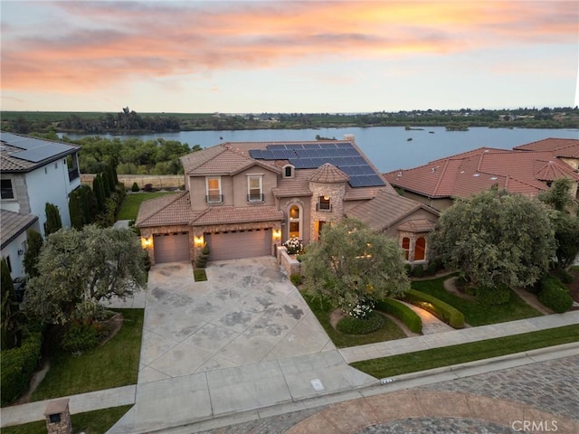 exterior space with stucco siding, a tiled roof, a water view, solar panels, and concrete driveway