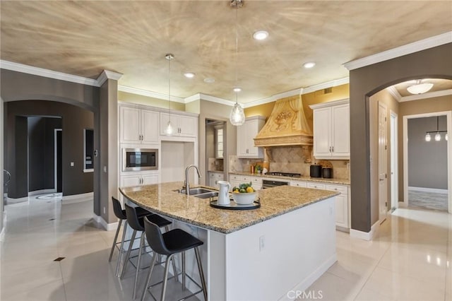 kitchen with arched walkways, a sink, custom range hood, and stainless steel appliances