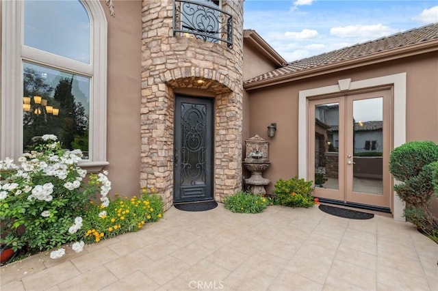 doorway to property featuring stone siding, stucco siding, french doors, and a patio area