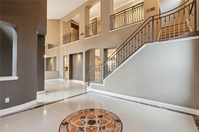 tiled entrance foyer with a towering ceiling, visible vents, stairway, and baseboards